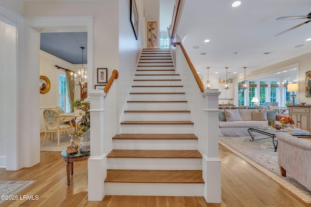 staircase featuring recessed lighting, wood finished floors, ornamental molding, and ceiling fan with notable chandelier