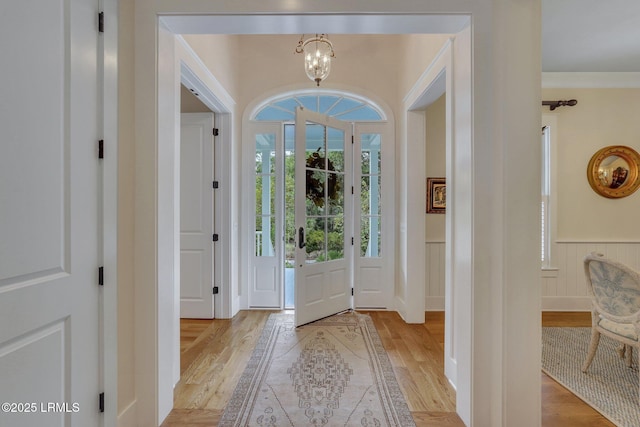 entrance foyer featuring light wood-type flooring, an inviting chandelier, wainscoting, and crown molding