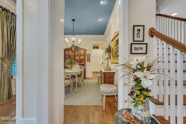 hall featuring a chandelier, wood finished floors, ornamental molding, and stairs