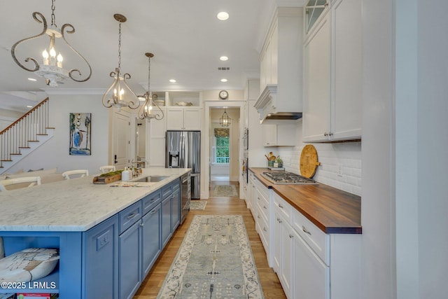 kitchen featuring blue cabinetry, butcher block countertops, decorative backsplash, appliances with stainless steel finishes, and white cabinetry