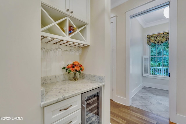 bar with baseboards, light wood finished floors, ornamental molding, a bar, and wine cooler