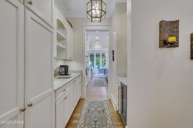 bar with beverage cooler, light wood finished floors, a sink, hanging light fixtures, and crown molding