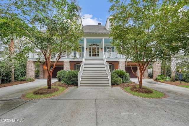 view of front facade featuring curved driveway, a porch, stairway, brick siding, and a chimney