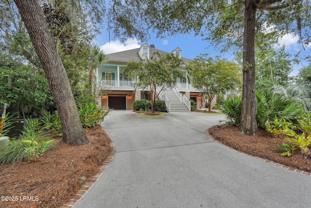 coastal home featuring stairway, covered porch, driveway, and an attached garage