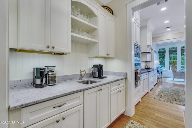 kitchen with light stone countertops, visible vents, a sink, light wood-style floors, and white cabinetry