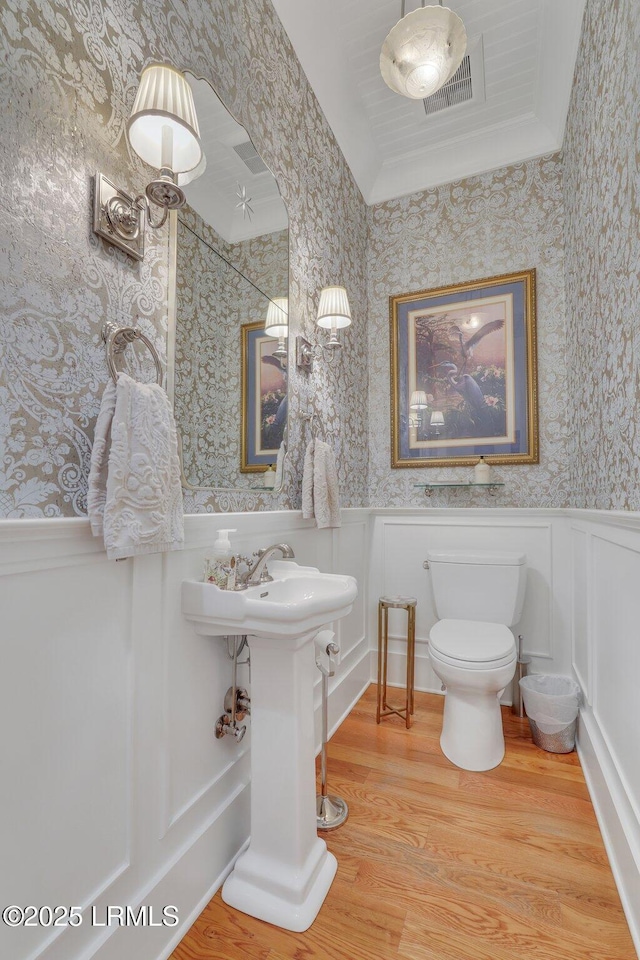 bathroom featuring visible vents, toilet, wood finished floors, wainscoting, and wallpapered walls