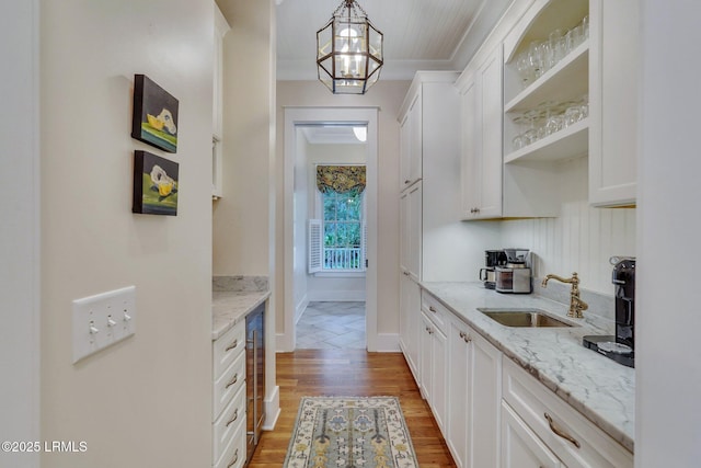 kitchen featuring light stone counters, white cabinetry, light wood-type flooring, and a sink