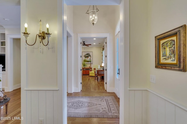 hall featuring an inviting chandelier, wood finished floors, and wainscoting