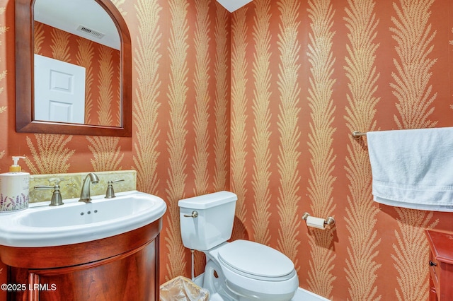 half bathroom featuring visible vents, vanity, toilet, and wallpapered walls