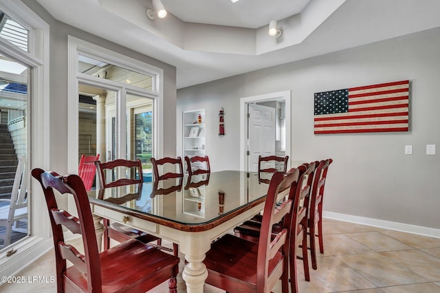 dining room featuring light tile patterned floors, baseboards, and a tray ceiling