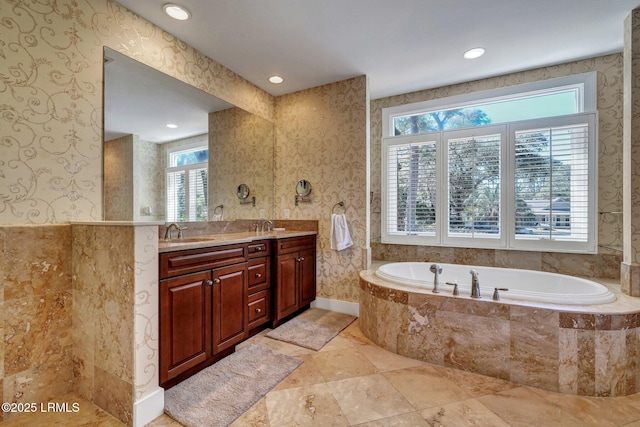 bathroom with double vanity, a sink, a bath, and wallpapered walls