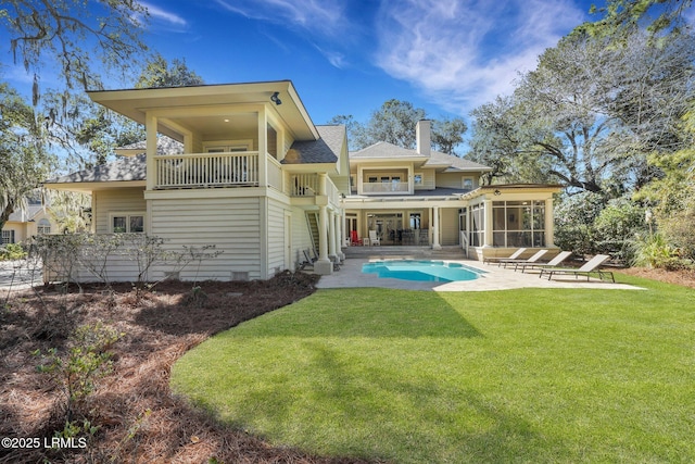 back of property with a lawn, a balcony, a sunroom, a chimney, and a patio area