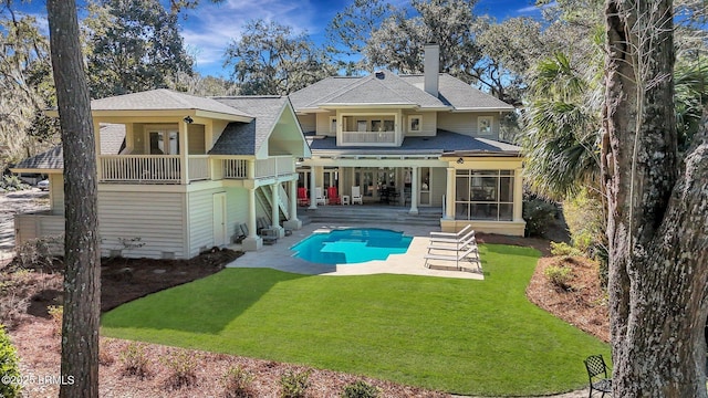 back of property with a patio, a balcony, a lawn, an outdoor pool, and a chimney