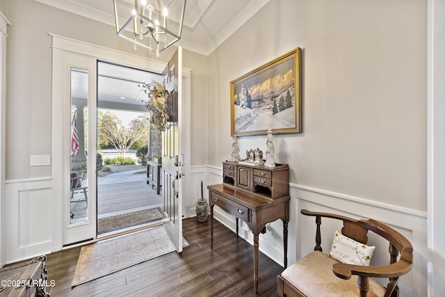 entryway featuring dark wood finished floors, wainscoting, ornamental molding, an inviting chandelier, and a decorative wall