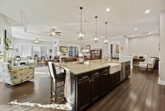 kitchen with sink, a breakfast bar area, hanging light fixtures, dark wood-type flooring, and a center island with sink