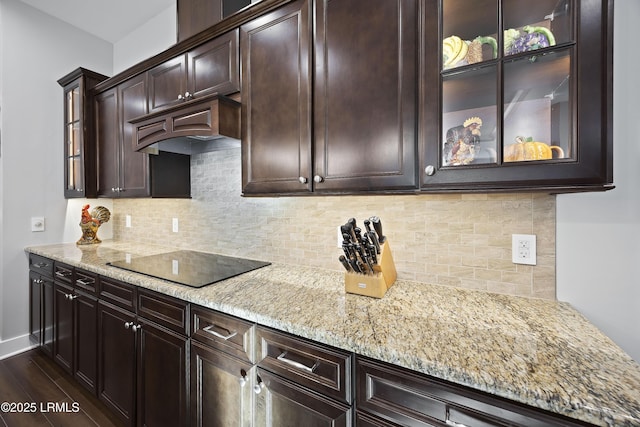 kitchen with black electric cooktop, light stone countertops, dark brown cabinets, decorative backsplash, and glass insert cabinets