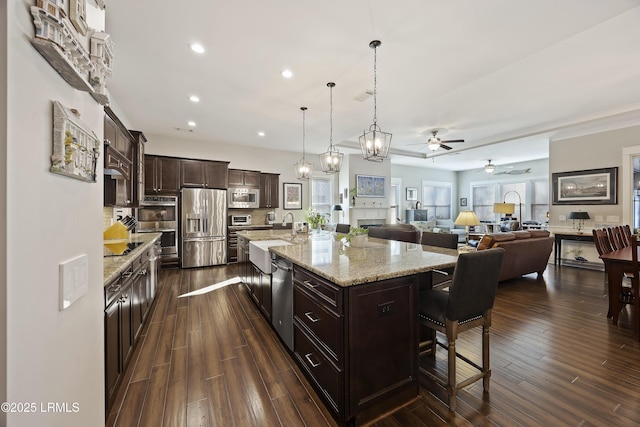 kitchen with decorative light fixtures, a breakfast bar area, a large island with sink, stainless steel appliances, and dark brown cabinets