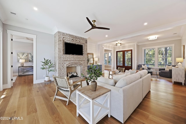 living room featuring crown molding, ceiling fan, a fireplace, and light hardwood / wood-style flooring