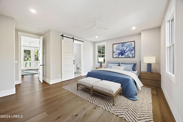 bedroom with dark wood-type flooring, a barn door, ceiling fan, and ensuite bathroom