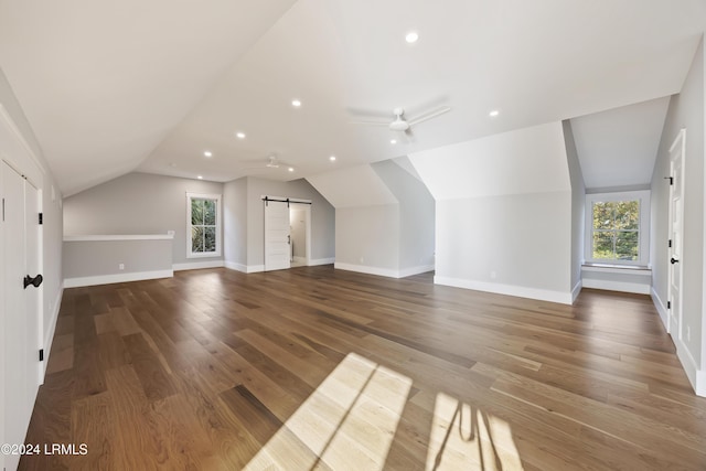 additional living space featuring vaulted ceiling, a barn door, dark wood-type flooring, and ceiling fan