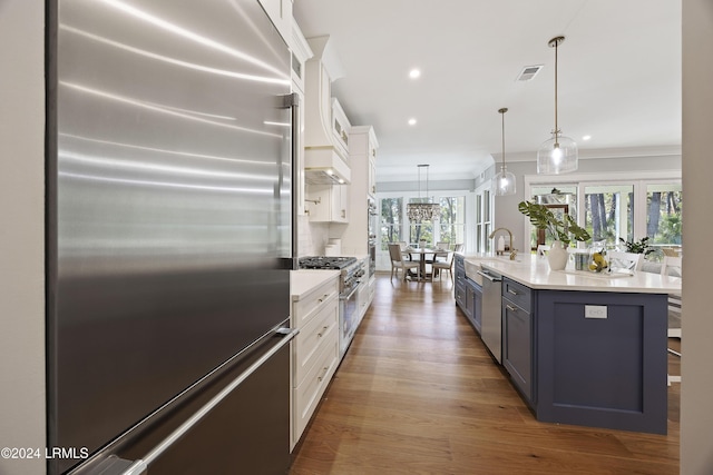 kitchen featuring decorative light fixtures, premium appliances, plenty of natural light, an island with sink, and white cabinets