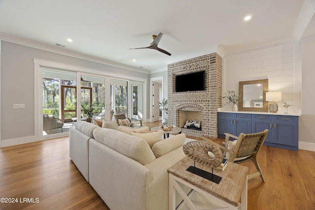 living room featuring ceiling fan, ornamental molding, a fireplace, and light hardwood / wood-style flooring