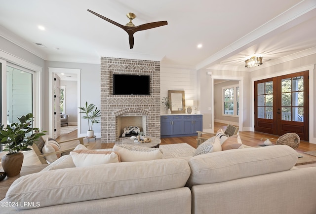 living room featuring ornamental molding, ceiling fan, light hardwood / wood-style floors, a brick fireplace, and french doors