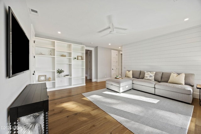 living room featuring wood-type flooring, wooden walls, and ceiling fan