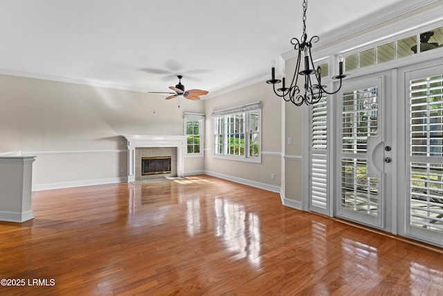 unfurnished living room with ornamental molding, ceiling fan with notable chandelier, wood finished floors, baseboards, and a tile fireplace