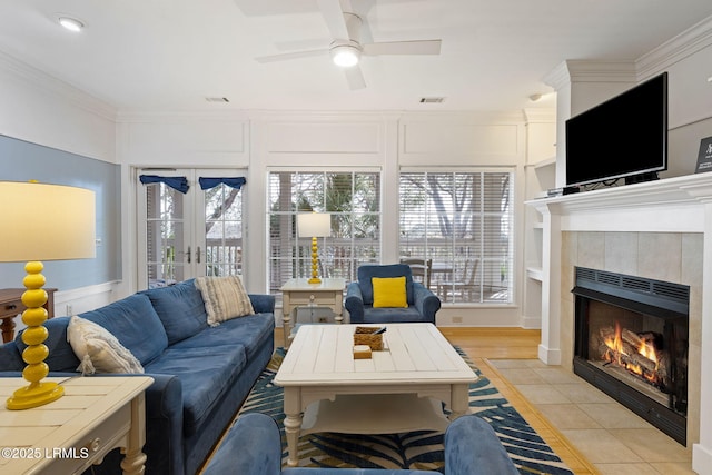 living room with crown molding, a tiled fireplace, french doors, and a wealth of natural light