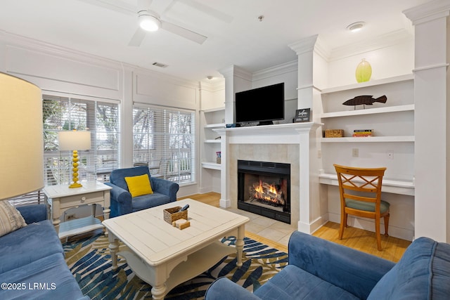 living room featuring a tile fireplace, crown molding, light hardwood / wood-style flooring, and built in shelves