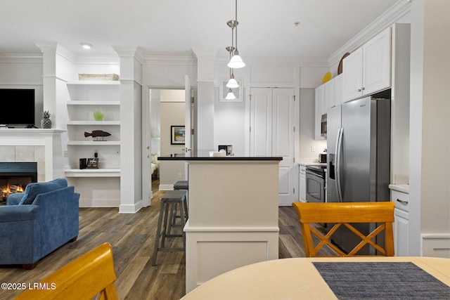 kitchen featuring appliances with stainless steel finishes, a fireplace, hanging light fixtures, ornamental molding, and a center island