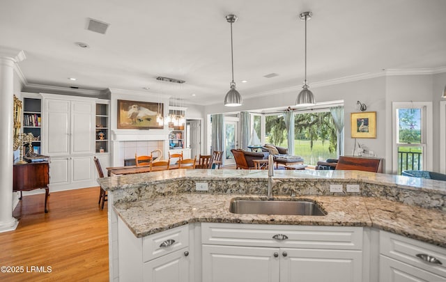 5 Petigru Dr, Beaufort, SC 29902 - kitchen with light wood finished floors, hanging light fixtures, white cabinets, crown molding, and light stone countertops