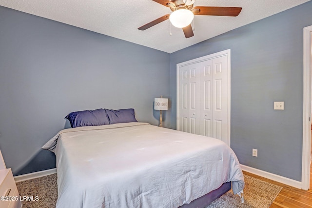 bedroom featuring ceiling fan, a textured ceiling, light wood-style floors, baseboards, and a closet