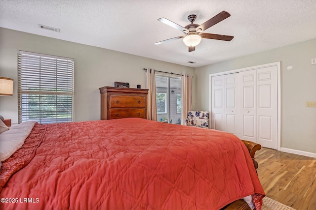 bedroom with baseboards, visible vents, a ceiling fan, wood finished floors, and a textured ceiling