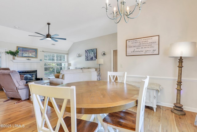 dining area featuring baseboards, lofted ceiling, ceiling fan, light wood-style floors, and a fireplace