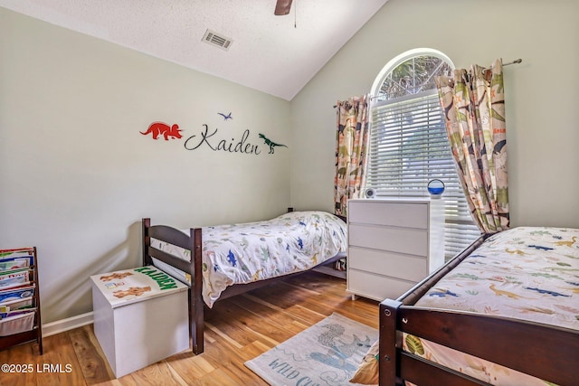 bedroom featuring light wood finished floors, visible vents, a ceiling fan, vaulted ceiling, and a textured ceiling