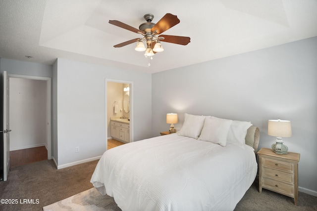 carpeted bedroom featuring ensuite bathroom, ceiling fan, and a tray ceiling