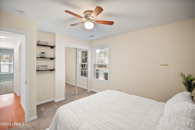 bedroom featuring ceiling fan, light colored carpet, multiple windows, and a textured ceiling