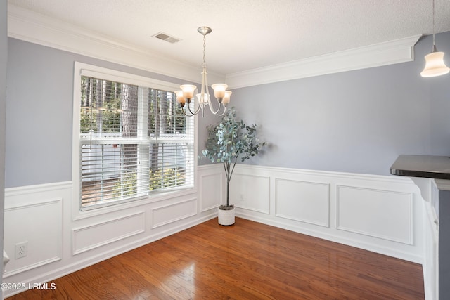 unfurnished dining area with an inviting chandelier, wood-type flooring, ornamental molding, and a textured ceiling