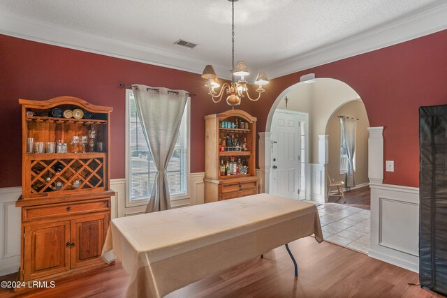 dining area featuring an inviting chandelier, ornamental molding, a textured ceiling, and light wood-type flooring