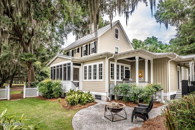 rear view of property featuring a lawn, a sunroom, and an outdoor fire pit