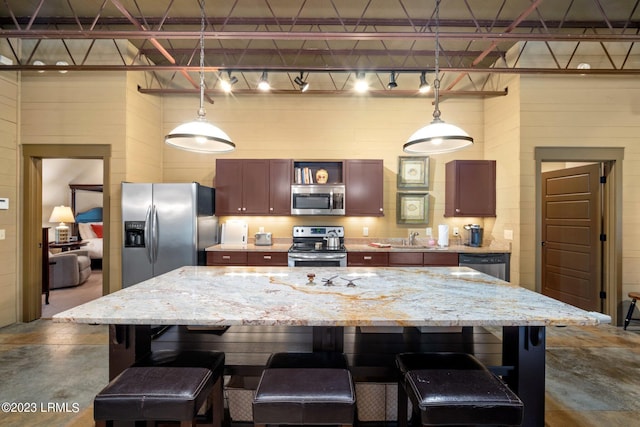 kitchen with hanging light fixtures, appliances with stainless steel finishes, a breakfast bar, and concrete floors