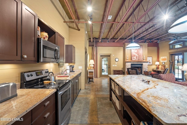 kitchen with hanging light fixtures, dark brown cabinetry, stainless steel appliances, light stone countertops, and a brick fireplace