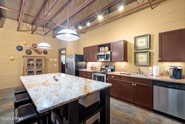 kitchen featuring sink, wood walls, light stone counters, hanging light fixtures, and stainless steel appliances