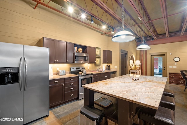 kitchen with a kitchen island, appliances with stainless steel finishes, a breakfast bar, pendant lighting, and light stone counters