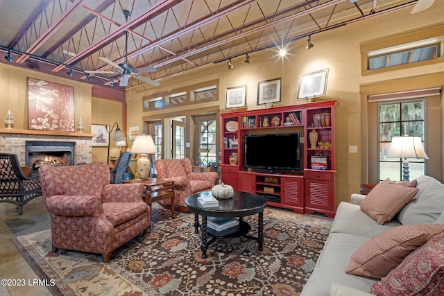 living room with rail lighting, ceiling fan, beam ceiling, wooden walls, and a brick fireplace