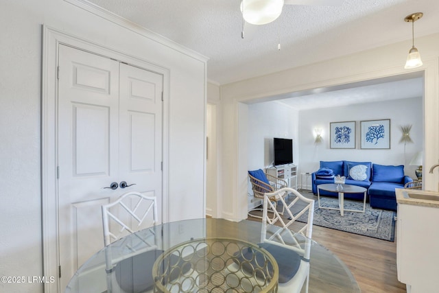 dining room featuring ceiling fan, ornamental molding, hardwood / wood-style floors, and a textured ceiling