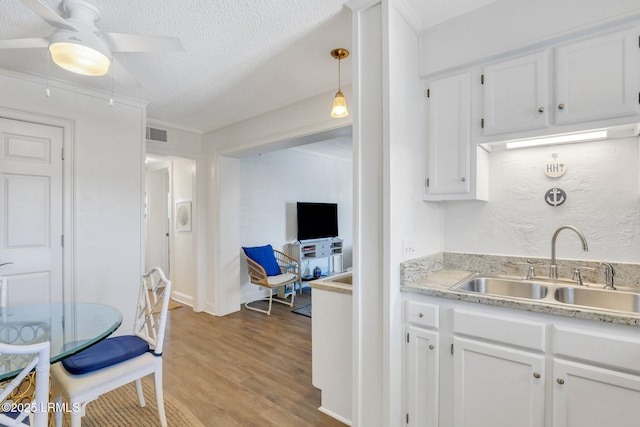 kitchen with hanging light fixtures, light hardwood / wood-style flooring, sink, and white cabinets