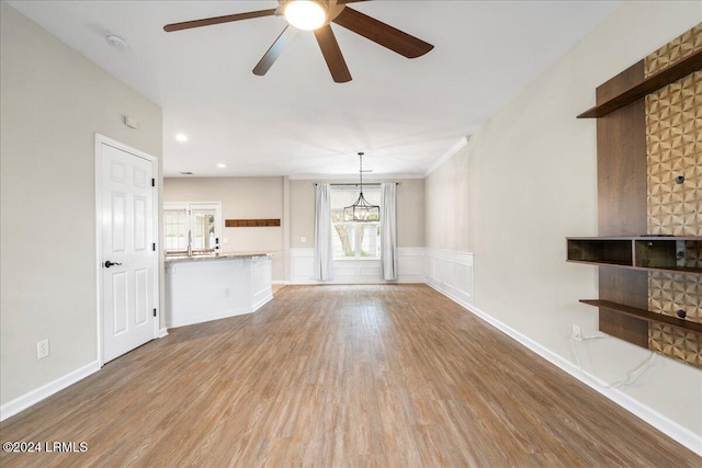 unfurnished living room with sink, ceiling fan with notable chandelier, and light hardwood / wood-style flooring